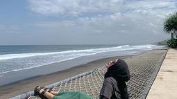 Mengenakan terusan hijau tua yang dikombinasikan dengan luaran hitam dan hijab berwarna senada, Putri Delina duduk di bibir laut beralaskan hammock. Ia menatap cakrawala yang memayungi laut. Bersama foto ini, ia mencuit soal kebahagiaan dan syukur, “Bukan kebahagiaan yang membuat kita bersyukur. Syukurlah yang membawa kita kepada kebahagiaan.” (Foto: Dok. Instagram @putridelinaa)