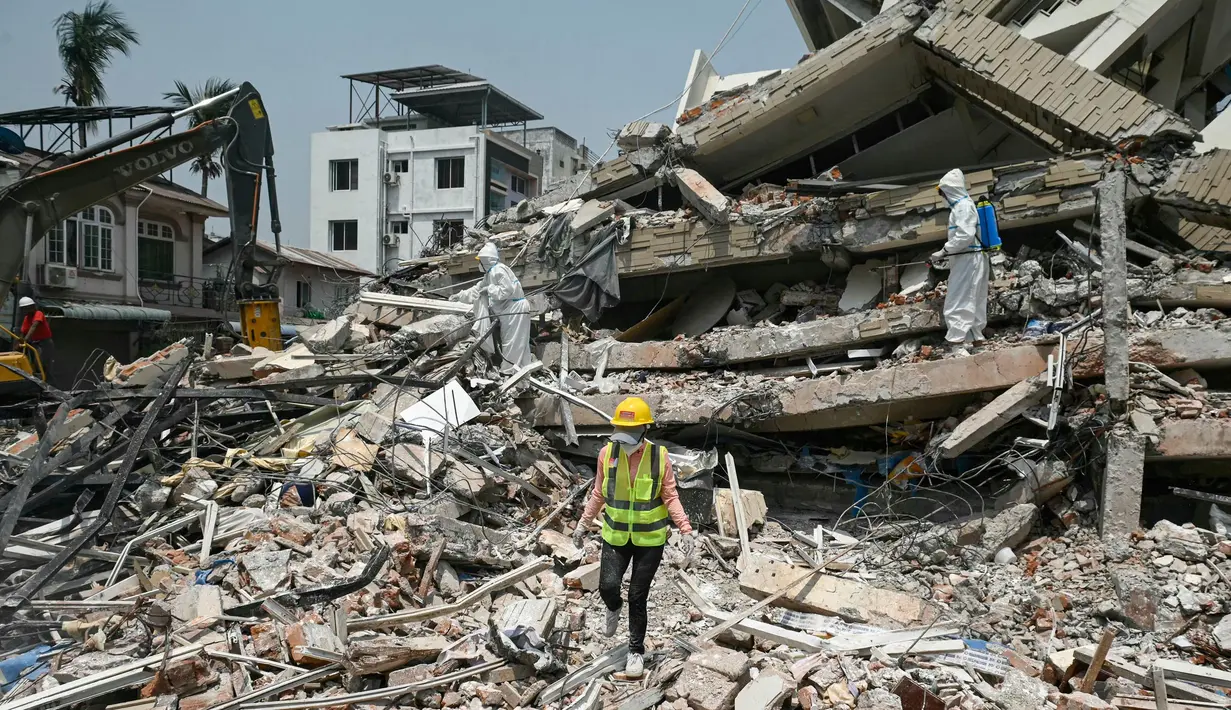 Para pekerja mengenakan pakaian hazmat menyemprotkan disinfektan untuk mensterilkan puing-puing bangunan yang runtuh di Mandalay pada 2 April 2025. (Sai Aung MAIN/AFP)