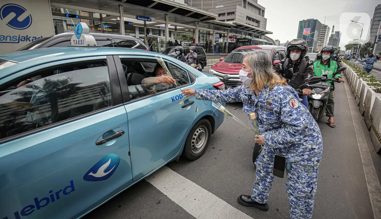 Perserta yang tergabung dalam Forum Kader Bela Negara DKI Jakarta membagikan bunga dan masker kepada pengguna jalan di Jalan Thamrin, Jakarta, Rabu (22/12/2021). Aksi tersebut merupakan bentuk apresiasi terhadap kaum perempuan terutama pada peringatan Hari Ibu. (Liputan6.com/Faizal Fanani)