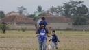 Seorang ayah menggendong anaknya saat melintasi sawah kering menuju Stadion Si Jalak Harupat, Bandung. (Bola.com/Vitalis Yogi Trisna)