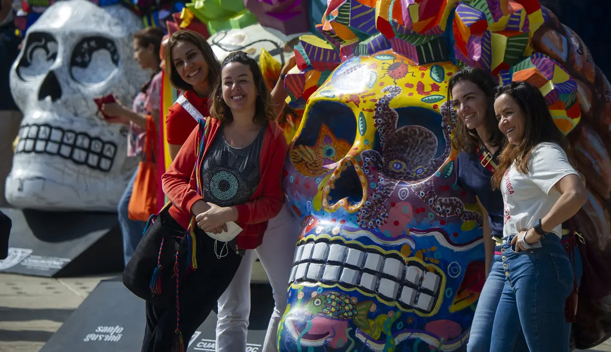 Para wanita berpose pada pameran Fridacraneos, tengkorak raksasa yang dilukis untuk menghormati mendiang seniman Meksiko Frida Kahlo, sebagai bagian dari perayaan Hari Kematian di Monumen Revolusi, Mexico City, Meksiko, 29 Oktober 2021. (Claudio CRUZ/AFP)
