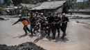 Warga menggunakan kayu untuk memindahkan sepeda motor melalui jalan banjir di Dusun Kamar Kajang, Lumajang, Kamis (9/12/2021). Luapan air sungai bercampur material lahar dingin erupsi Gunung Semeru merendam puluhan rumah akibat diguyur hujan deras pada Selasa dan Rabu malam. (Juni Kriswanto/AFP)