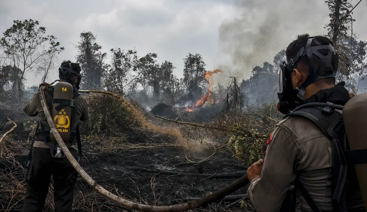Polisi yang mengenakan perlengkapan pemadam kebakaran memadamkan kebakaran lahan gambut di Tambang, Kabupaten Kampar, Provinsi Riau, Selasa,  25 Agustus 2026. (AFP/ Wahyudi)