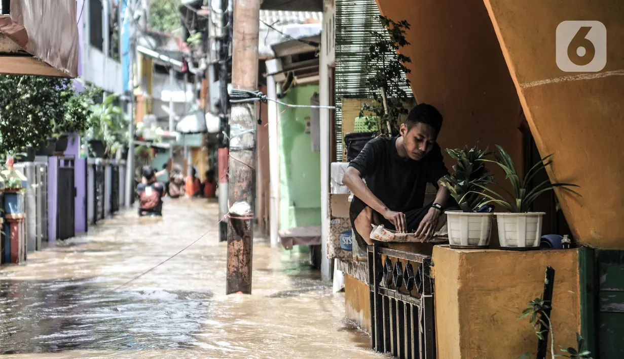 Warga makan di atas pagar rumah saat banjir merendam permukiman di Kebon Pala, Jakarta, Senin (8/2/2021). Hujan deras yang mengguyur Ibu Kota dan wilayah Bogor menyebabkan permukiman di Kebon Pala terendam banjir sejak Minggu (7/2/2021) sore. (merdeka.com/Iqbal S. Nugroho)