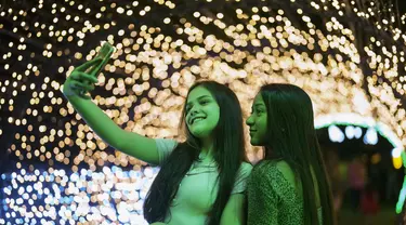 Dua wanita berfoto selfie di acara lampu Natal di taman Ibirapuera di Sao Paulo, Brasil, Selasa (14/12/2021). Jelang perayaan Natal, taman dan pantai dihiasi lampu-lampu yang indah. (AP Photo/Andre Penner)