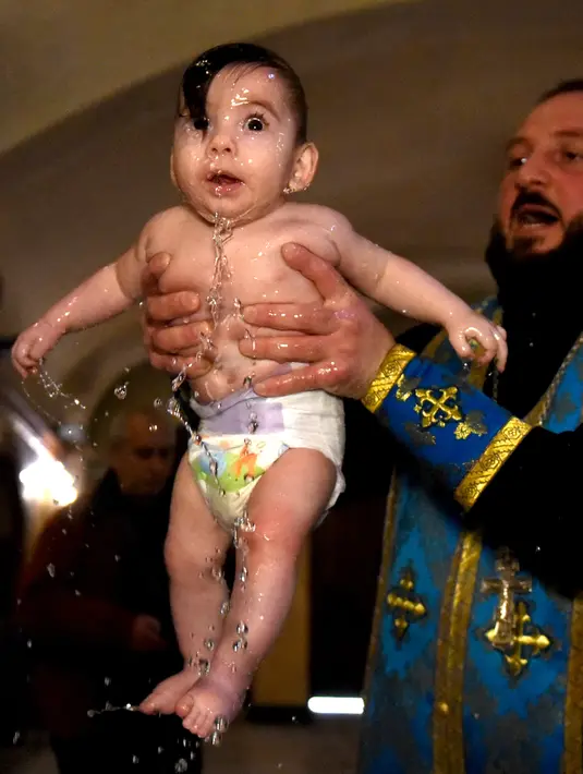 Ekspresi seorang bayi saat pendeta mengangkatnya dari air dalam acara pembaptisan massal di Gereja Katedral Holy Trinity, Tbilisi, Georgia (21/1). (AFP Photo/Vano Shlamov)