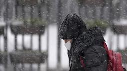 Seorang perempuan mengenakan masker berjalan melalui jalan yang tertutup salju di Beograd, Serbia, Minggu (12/12/2021). Di ibu kota Serbia, beberapa pohon tumbang karena beratnya tumpukan salju, merusak mobil dan bangunan. (AP Photo/Darko Vojinovic)