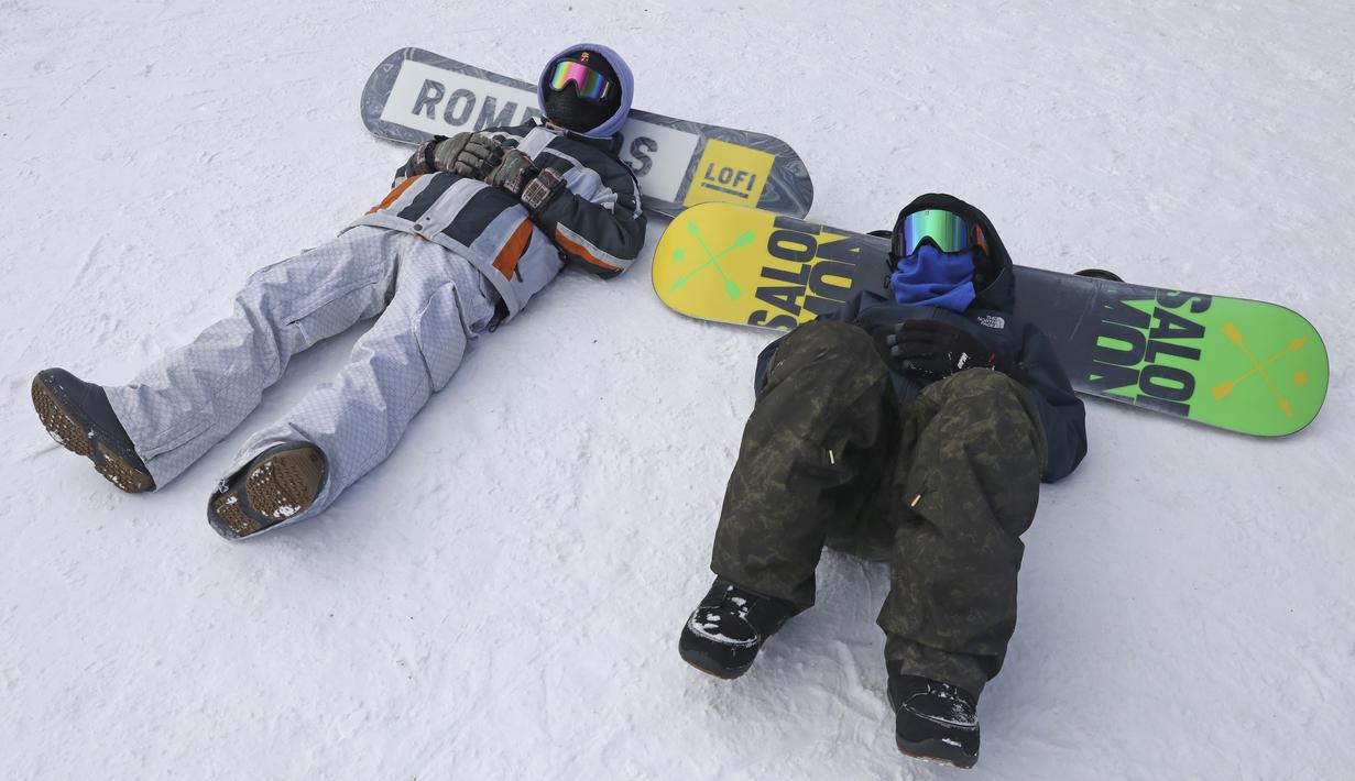 Snowboarders beristirahat di dasar lereng di resor ski Tochal di luar ibukota Teheran, Iran (1/1/2022). Di tengah polusi udara dan kesengsaraan ekonomi, penduduk Teheran menemukan kenyamanan di resor ski di utara Teheran di pegunungan Alborz. (AP Photo/Vahid Salemi)