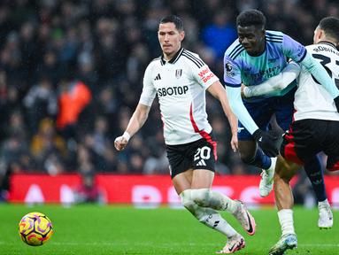Pemain Fulham, Antonee Robinson, berusaha mengadang pergerakan pemain Arsenal, Bukayo Saka dalam lanjutan Liga Inggris di Craven Cottage, Minggu (9/12/2024). (AFP/Justin Tallis)
