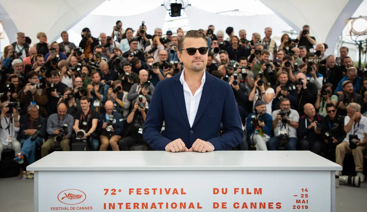 Aktor Leonardo DiCaprio berpose saat menghadiri pemutaran film 'Once Upon a Time in Hollywood' selama Festival Film Cannes Internasional ke-72 di Prancis (22/5/2019). DiCaprio tampil dengan setelan jas biru necis dan kemeja putih dengan bagian atas tanpa dikancing. (AP Photo/Vianney Le Caer