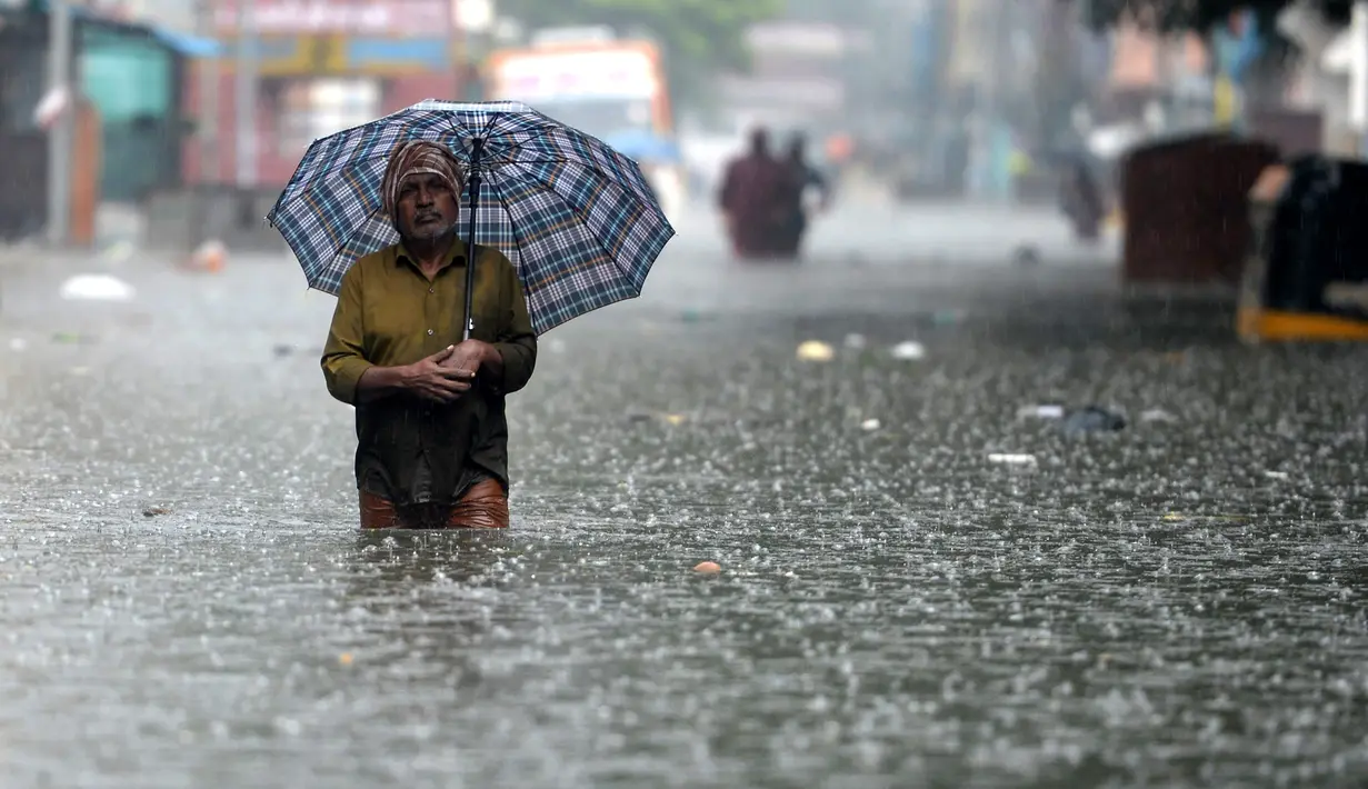 Orang-orang mengarungi jalan yang banjir setelah hujan lebat di Chennai, India (8/11/2021). Hujan lebat terus menyebabkan genangan air di Chennai dan daerah sekitarnya. (AFP/Arun Sankar)