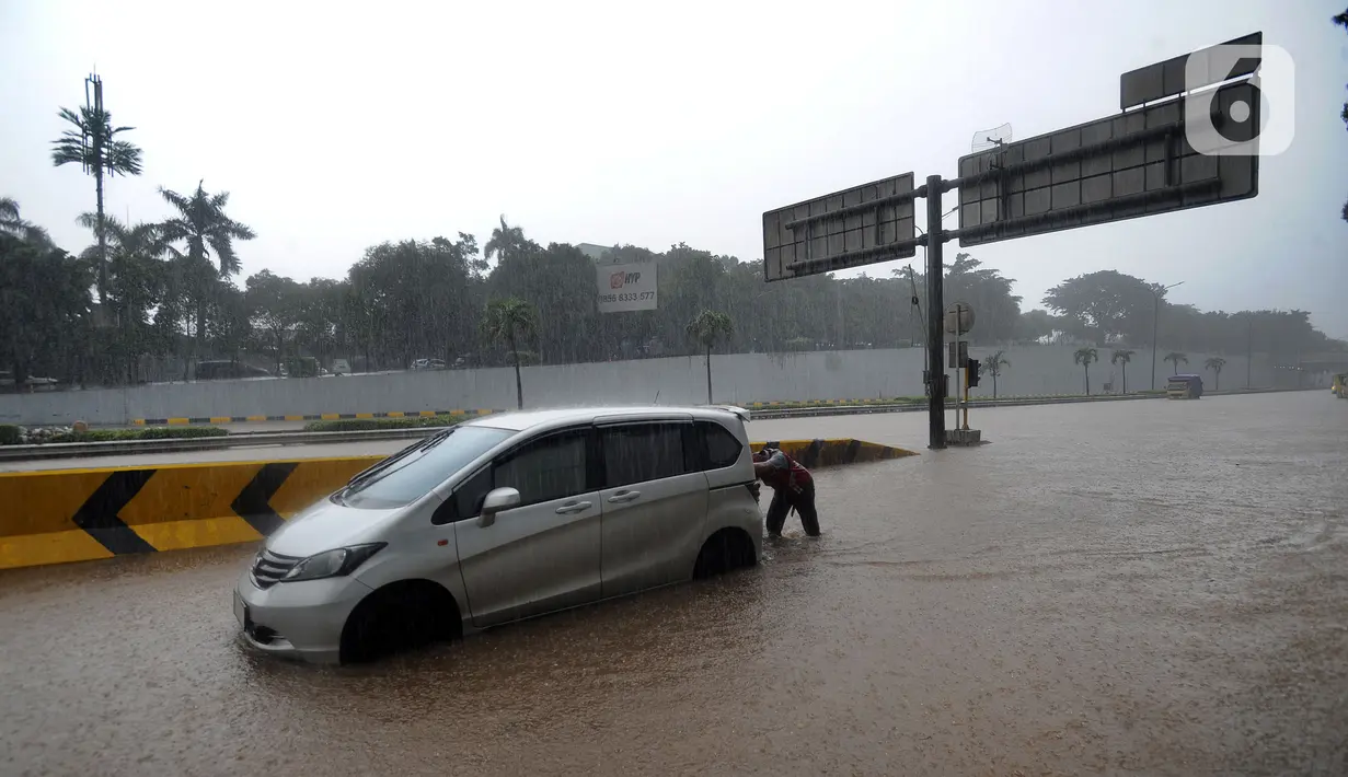 Seorang pria mendorong mobil yang mogok saat banjir menggenangi Jalan Tol JORR di kawasan TB Simatupang, Jakarta Selatan, Sabtu (20/2/2021). Banjir terjadi akibat luapan Kali Serua yang berada di pinggir jalan tol. (merdeka.com/Arie Basuki)