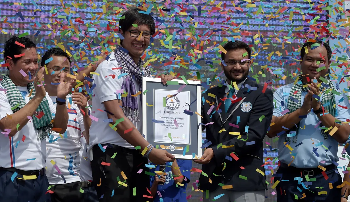 Juri Guinness, Swapnil Dangarikar memberikan sertifikat kepada gerakan GoGo Cambodia, Sann Vathana setelah syal krama sepanjang 1,149.8 meter memecahkan rekor sebagai syal tenun terpanjang dunia di Phnom Penh, Kamboja, Minggu (1/7). (AFP/TANG CHHIN Sothy)