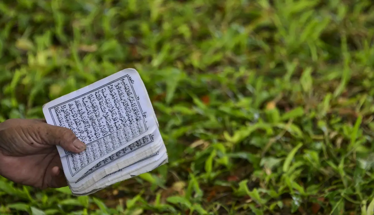 Seorang perempuan membaca Alquran pada peringatan 16 tahun gempa bumi dan tsunami Aceh di sebuah kuburan massal di Siron, Sabtu (26/12/2020).  Peringatan di tengah pandemi COVID-19 itu tetap berlangsung secara sederhana melalui kegiatan ziarah kubur. (CHAIDEER MAHYUDDIN/AFP)
