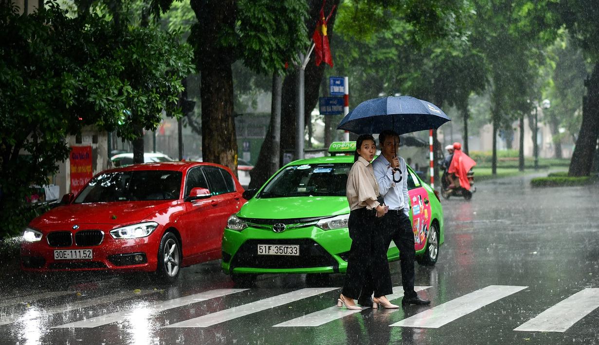 Pejalan kaki menyeberang jalan saat hujan deras di Hanoi (14/10/2020). Badai tropis Nangka menghantam Vietnam tengah-utara yang mengakibatkan bencana alam, terutama hujan lebat dan banjir, telah menyebabkan 28 orang tewas dan 12 lainnya hilang. (AFP Photo/Manan Vatsyayana)