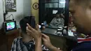 Tukang cukur rambut dan pelanggannya menyempatkan menonton pertandingan Timnas Indonesia vs Australia pada babak 16 besar Piala Asia di kawasan Pinang, Tangerang, Minggu (28/1/2024). Indonesia tumbang empat gol tanpa balas. (Bola.com/M Iqbal Ichsan)