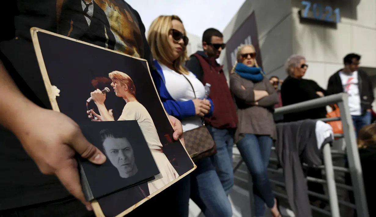 Penggemar membawa foto David Bowie  saat berkumpul di dekat bintang atas nama penyanyi legendaris itu di Hollywood Walk of Fame di Los Angeles, Senin (11/1). Bowie meninggal di usia 69 tahun dan baru saja merilis album ke-25 nya. (REUTERS/ Mario Anzuoni)
