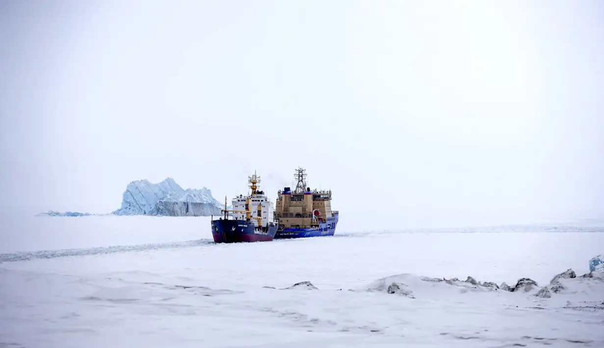 Kapal pemecah es membuat jalur untuk kapal kargo dengan latar belakang gunung es dekat pelabuhan di Pulau Alexandra Land dekat Nagurskoye, Rusia, Senin (17/5/2021). Pulau Alexandra Land merupakan pangkalan militer paling utara Rusia. (AP Photo/Alexander Zemlianichenko)