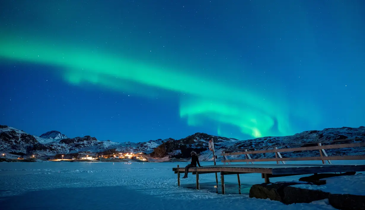 Seorang wanita duduk di dermaga untuk menonton Aurora Borealis atau Northern Lights di di Kepulauan Lofoten, Bostad, lingkaran Arktik, Norwegia, Sabtu (3/3). Cahaya Aurora biasa terlihat di sekitar daerah Kutub Utara dan Selatan. (Olivier MORIN/AFP)