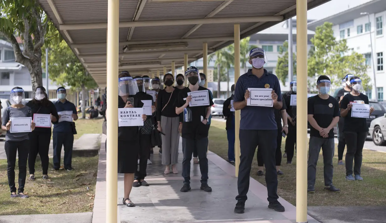 Dokter kontrak memegang plakat saat berpartisipasi dalam aksi mogok di Rumah Sakit Sungai Buloh di Selangor, Malaysia, Senin (26/7/2021). Ratusan dokter melakukan aksi mogok kerja dari rumah sakit pemerintah Malaysia pada (26/7). (AFP/Arif Kartono)
