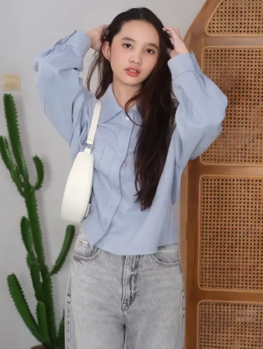 Rambut panjang ditata tanpa poni yang menampilkan keningnya. Ia tampil mengenakan kemeja biru dipadukan celana denim panjangnya. [@kana.sybilla]