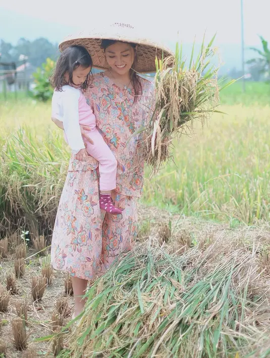 Seperti ibu petani, sambil mengendong putrinya, Thalia dengan mengenakan caping. Menurutnya, ini salah satu caranya untuk mengenalkan padi pada putrinya sebelum akhirnya menjadi beras dan nasi untuk dimakan. (Instagram/ruben_onsu)