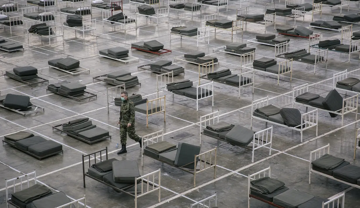 Tentara Serbia berjalan di antara tempat tidur di dalam aula Belgrade Fair yang diubah menjadi rumah sakit sementara virus Corona, Selasa (24/3/2020). Sebanyak 3000 tempat tidur disiapkan untuk  menangani pasien dengan gejala ringan corona Covid-19. (Vladimir Zivojinovic/AFP)