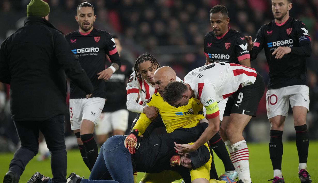 <p>Kiper Sevilla, Marko Dmitrovic berhasil melumpuhkan seorang suporter fanatik PSV yang menyerangnya dalam laga leg kedua babak playoff fase gugur Liga Europa 2022/2023 di Philips Stadium, Eindhoven, Jumat (24/2/2023). (AP Photo/Peter Dejong)</p>