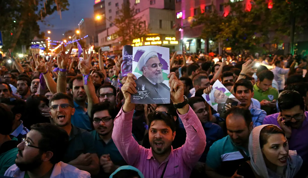 Seorang pendukung Presiden Iran Hassan Rouhani membawa poster saat merayakan kemenangannya dalam pemilihan presiden Iran di Teheran, Iran (20/5). (AP Photo/Ebrahim Noroozi)