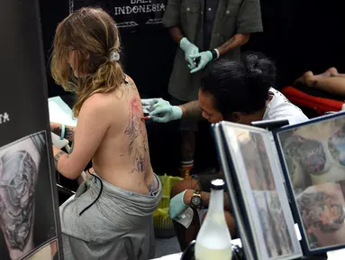 Seorang wanita saat dibuatkan tato dibagian punggung oleh seniman dalam acara Bali Tattoo Expo 2017 di pulau resor Indonesia, Denpasar, Bali (12/5). Acara ini digelar selama 3 hari, mulai (12/5/2017) sampai (14/5/2017). (AFP Photo/Sonny Tumbelaka)