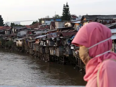 Warga melintas di jembatan berlatar pemukiman di kawasan bantaran Kali Ciliwung, Jakarta, Rabu (10/3/2021). Wagub DKI Jakarta Ahmad Riza Patria mengungkap dua kendala terkait pembebasan lahan untuk normalisasi Sungai Ciliwung sebagai upaya mencegah banjir. (Liputan6.com/Helmi Fithriansyah)