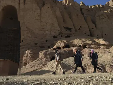 Orang-orang Hazara berjalan di situs patung Buddha raksasa yang dihancurkan oleh Taliban pada 2001 di Provinsi Bamiyan, Afghanistan, 3 Maret 2021. Terletak di jantung pegunungan Hindu Kush, di tebing indah lembah Bamiyan terdapat gua yang berisi kuil, biara, dan lukisan Buddha. (BANGUN KOHSAR/AFP)