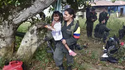 Seorang gerilyawati FARC menggendong seorang anak di kamp Magdalena Medio, Kolombia (15/3/2016). Gerilyawati FARC dikenal lebih sadis terhadap musuh daripada pasukan gerilyawan. (AFP Photo/Luis Acosta)