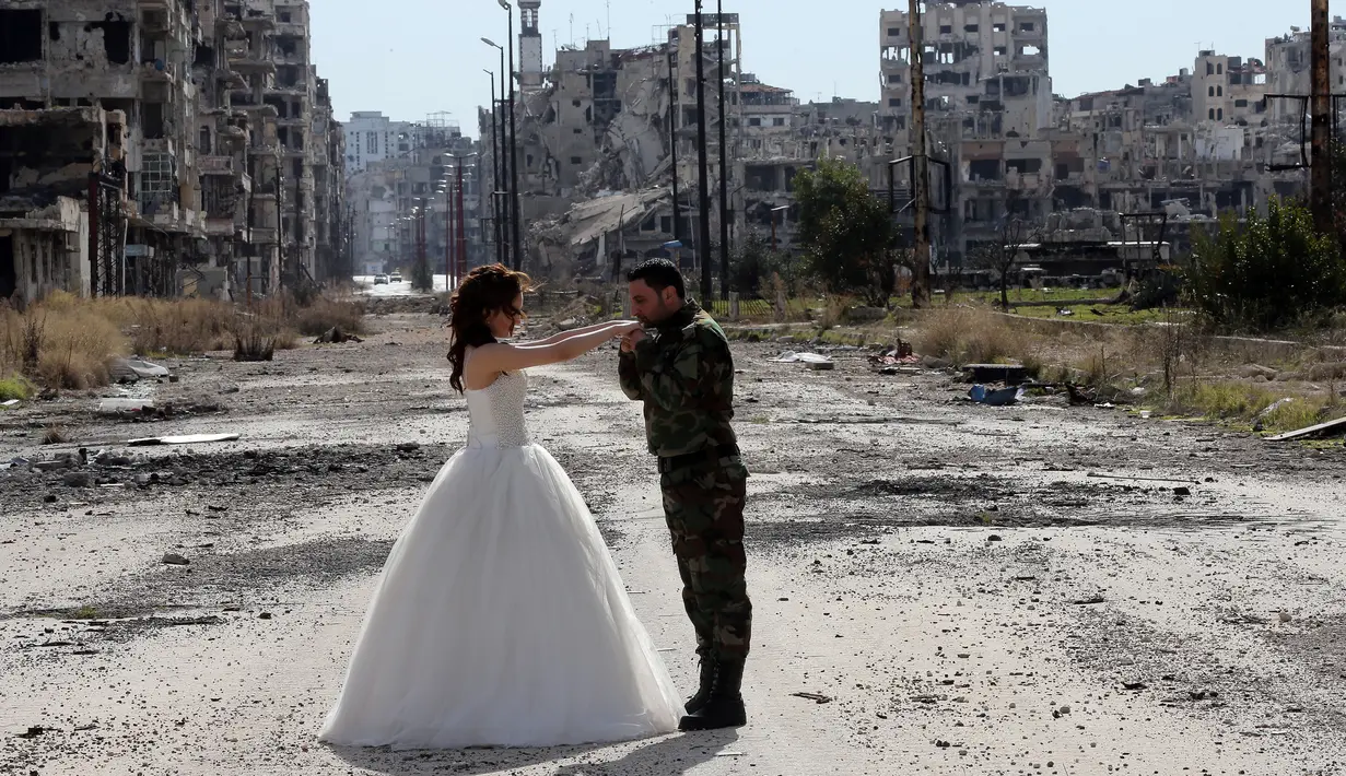 Pasangan pengantin baru, Hassan Youssef (27) tampak menghadap  pengantin wanita, Nada Merhi (18), sambil mencium tangan pasangannya dengan latar belakang pemandangan tandus kota Homs yang menjadi medan perang di Suriah, 5 Februari 2016. (JOSEPH EID/AFP)