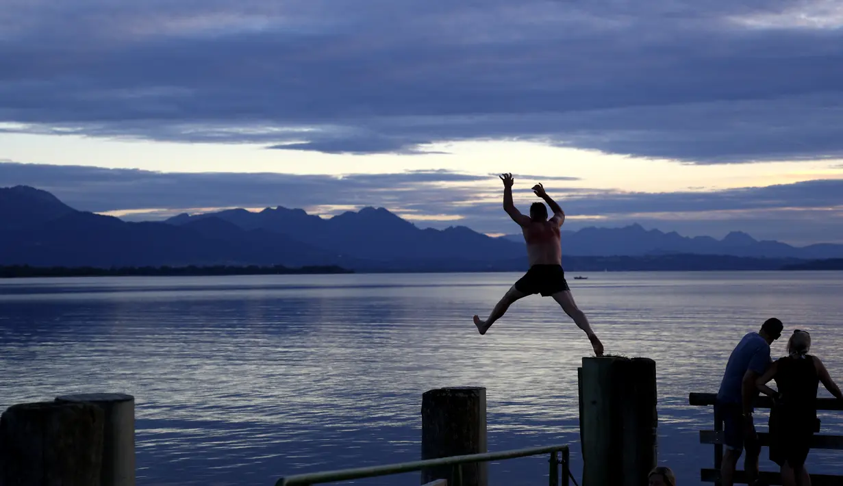 Seorang pria melompat ke danau Chiemsee saat matahari terbenam di Chieming, Jerman, Selasa, (25/8/2020). Chiemsee terbentuk pada akhir zaman es sekitar 10.000 tahun yang lalu dari lubang yang terbentuk oleh gletser yang mencair. (AP Photo / Matthias Schrader)