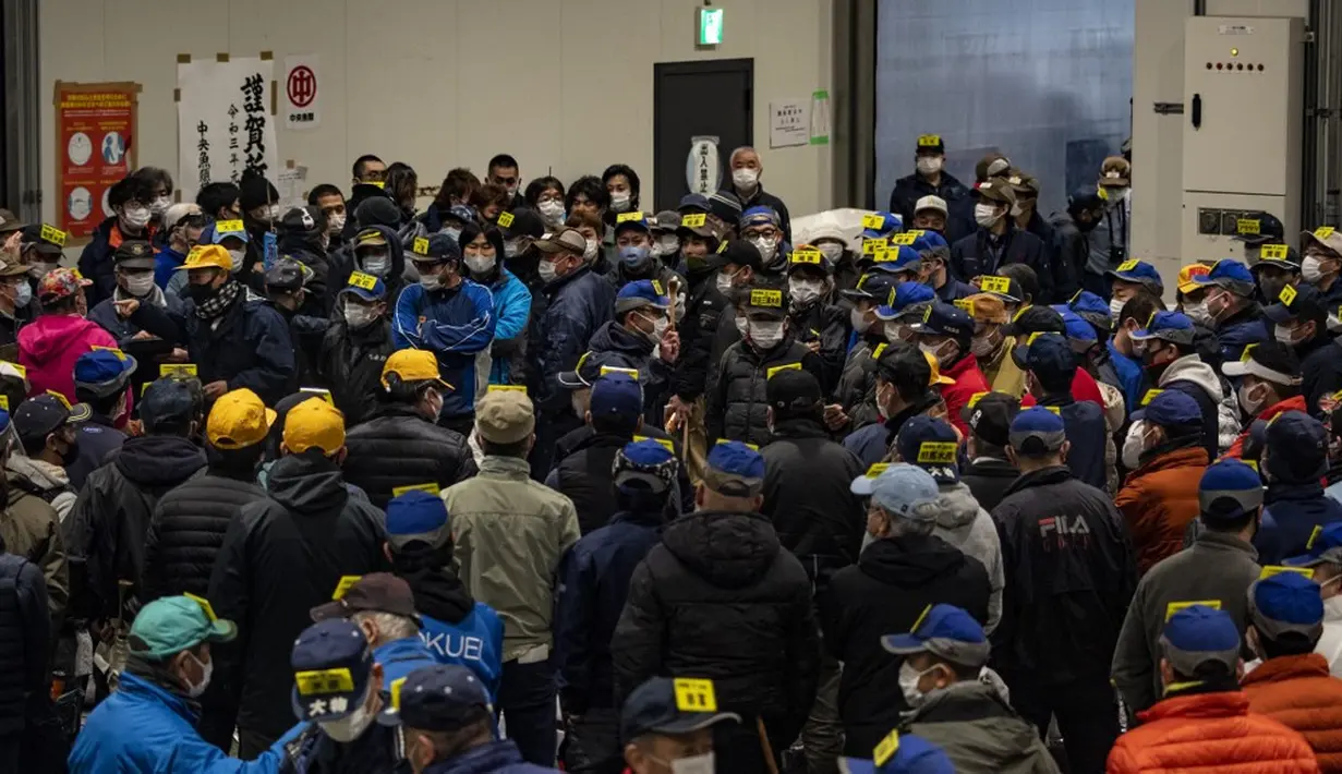 Para tengkulak yang mengenakan masker untuk mencegah penularan COVID-19 berpartisipasi dalam lelang tuna di Pasar Toyosu, Tokyo, Jepang, 5 Januari 2021. Untuk lelang tahun ini, para tengkulak diwajibkan menggunakan masker dan membersihkan tangan saat memeriksa tekstur tuna. (Philip FONG/AFP)