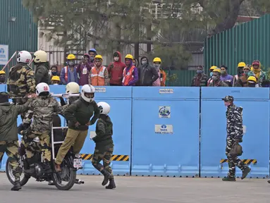 Pekerja menyaksikan pasukan pertahanan berlatih untuk parade Hari Republik mendatang di perbukitan Raisina, pusat kekuasaan pemerintah, di New Delhi, India (17/1/2022). India akan merayakan Hari Republik pada 26 Januari. (AP Photo/Manish Swarup)