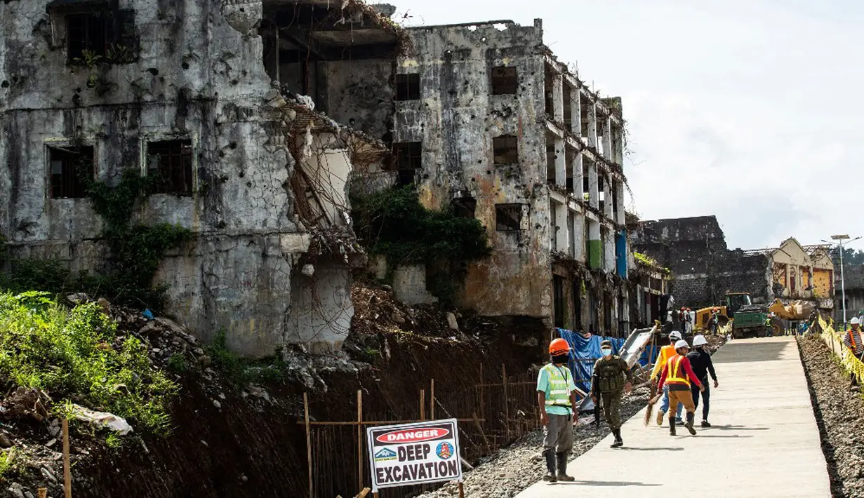 Para pekerja berjalan menyusuri jalan yang baru diaspal melewati rumah-rumah yang hancur saat pertempuran tentara pemerintah melawan ISIS di Kota Marawi, Mindanao, Filipina, 23 Mei 2021. (Ferdinandh CABRERA/AFP)