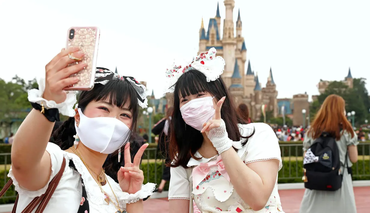 Pengunjung mengenakan masker guna melindungi diri dari virus corona berswafoto saat mengunjungi Tokyo Disneyland di Urayasu, dekat Tokyo, Rabu (1/7/2020). Tokyo Disneyland dibuka kembali untuk pertama kalinya dalam empat bulan setelah sempat ditutup karena penyebaran Covid-19. (AP/ Koji Sasahara)
