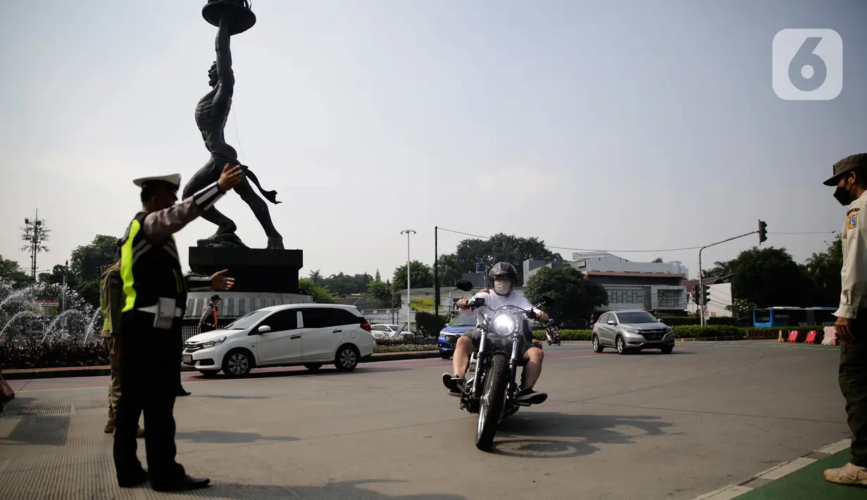 Petugas polisi mengarahkan kendaraan berplat nomor genap di pos penyekatan ganjil-genap di Bundaran Senayan, Minggu (5/9/2021). Pembatasan kendaraan dengan sistem pelat nomor kendaraan ini tetap berlaku di akhir pekan, Sabtu dan Minggu. (Liputan6.com/Angga Yuniar)