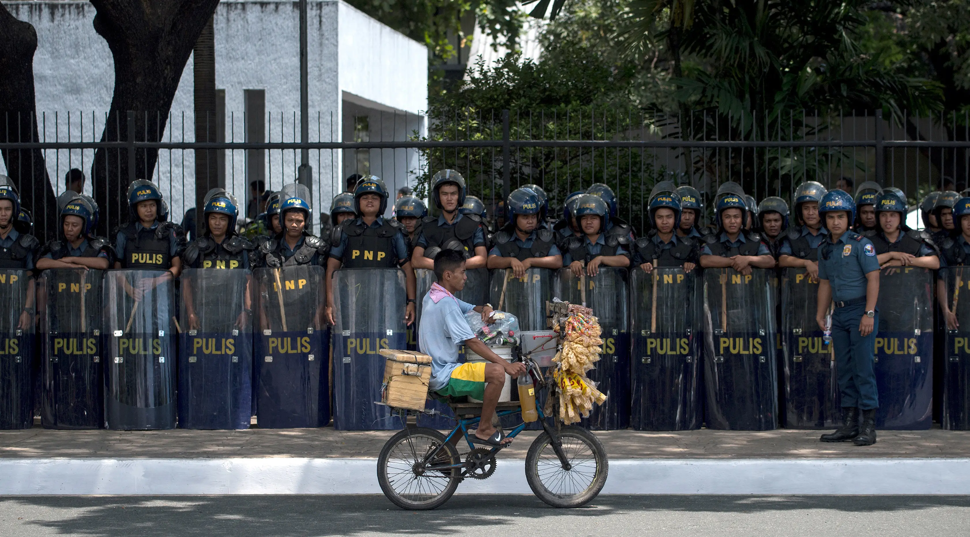 Seorang pedagang melintas di dekat polisi yang berjaga di lokasi pertemuan ASEAN di Manila Bay, Filipina, Rabu (26/4). Sekitar 40 ribu pasukan keamanan dikerahkan untuk menjaga acara tersebut. (AFP PHOTO / Noel CELIS)