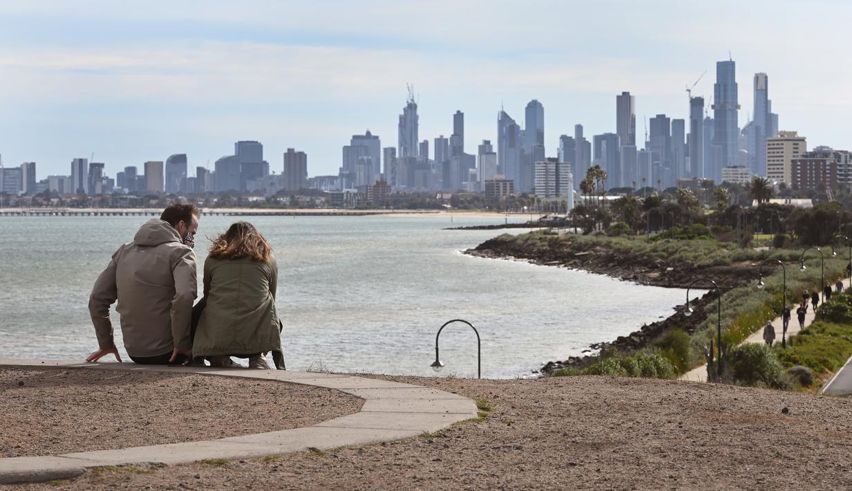 Suami istri beristirahat dari berolahraga dengan pemandangan cakrawala Melbourne (11/8/2020). Negara bagian Victoria melaporkan 19 kematian akibat virus corona pada 11 Agustus, menjadikannya hari yang sama mematikan bagi pandemi di negara itu meskipun jumlah kasus baru turun. (AFP/William West)