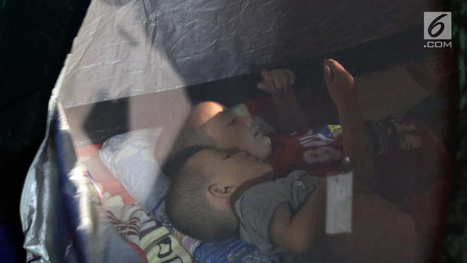 Dua anak pencari suaka bermain ponsel di dalam tenda yang dibangun di atas trotoar depan Masjid Ar-Rayan, Jalan Kebon Sirih, Jakarta, Jumat (5/7/2019). Para pencari suaka dari sejumlah negara berkonflik berharap UNHCR bisa segera memberikan jaminan perlindungan bagi mereka. (Liputan6.com/Helmi Fithr