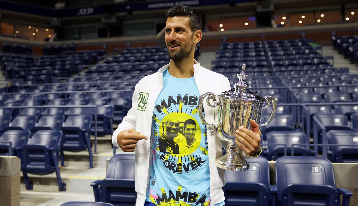 Novak Djokovic memamerkan pakaian yang digunakannya dengan gambar Kobe Bryant bersama dirinya dan tulisan "Mamba Forever" setelah keluar sebagai juara US Open 2023 yang berlangsung di Arthur Ashe, New York, Senin (11/9/2023) pagi WIB. (AFP/Getty Images/Clive Brunskill)