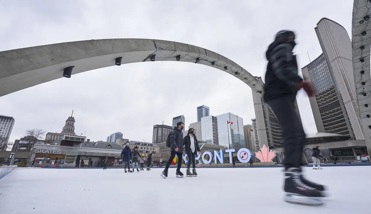 Orang-orang berseluncur es di arena luar ruangan di Nathan Phillips Square di Toronto, Ontario, Rabu (5/1/2022). Provinsi Ontario menutup semua arena dalam ruangan serta pusat kebugaran lainnya di tengah kesibukan pembatasan baru guna membendung penyebaran varian Omicron Covid-19. (Geoff Robins/AFP)