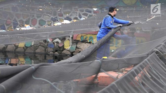 Petugas melepas kain waring atau jaring yang menutupi Kali Item di Kemayoran Jakarta, Rabu (14/11). Pelepasan waring yang sebagian dalam kondisi sudah robek itu dilakukan lantaran banyak warga yang membuang sampah di atasnya (Merdeka.com/Iqbal S. Nugroho)