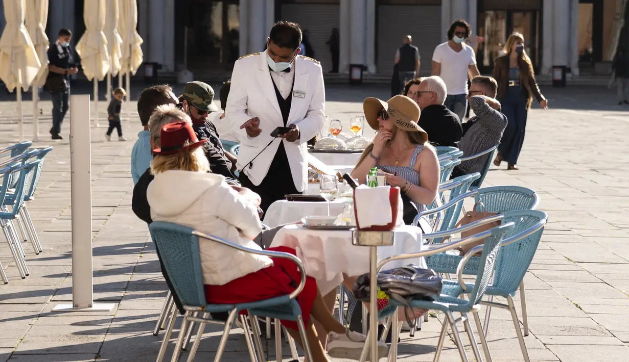 Pramusaji mengobrol dengan turis yang duduk di teras kafe Piazza San Marco di Venesia pada 20 Mei 2021. Turis kembali berdatangan menikmati keindahan Venesia, yang sering dijuluki kota paling romantis di dunia, setelah Italia menghapus kewajiban karantina bagi pendatang. (Marco Bertorello/AFP)