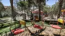 Seorang pekerja mengenakan masker menyiram tanah dan kursi komedi putar di kebun binatang lokal Palestina di Rafah di Jalur Gaza selatan (26/5/2020). Kebun binatang itu ditutup selama liburan Idul Fitri karena pandemi virus coronavirus COVID-19. (AFP/Said Khatib)