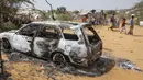 Warga berjalan melewati puing-puing kendaraan yang hancur dalam serangan terhadap polisi dan pos pemeriksaan di pinggiran ibu kota Mogadishu, Somalia (16/2/2022). Serangan oleh kelompok ekstremis al-Shabab pada hari Rabu menewaskan lima orang dan melukai 16 orang. (AP Photo/Farah Abdi Warsameh)