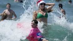 Pengunjung asal Inggris Sophie Woodward (kanan) mengenakan topi Santa saat bermain di air bersama sepupunya Maxi Woodward di Pantai Bondi di Sydney, Senin, 25 Desember 2023. (AP Photo/Rick Rycroft)
